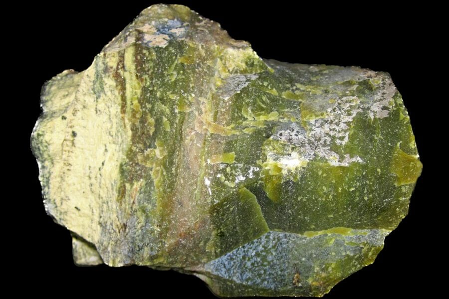 A bright light green Serpentine attached to a rock against a black background