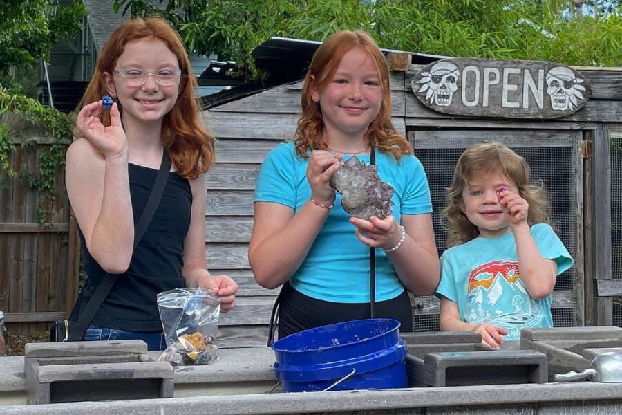 Three kids of different ages proudly showing the gems they sifted through the mining sluice of The Village Mystic