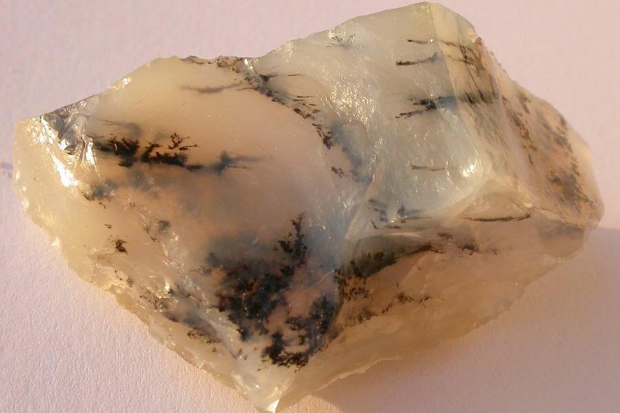 A white translucent Moss Opal laying on a light pink surface