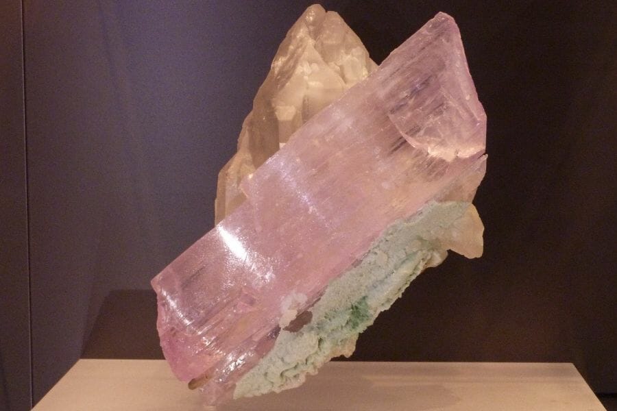 A translucent light pink Spodumene atop a rock on a wooden surface