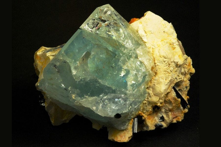 An ethereal blue Topaz, the state gemstone, attached to a rock against a black background