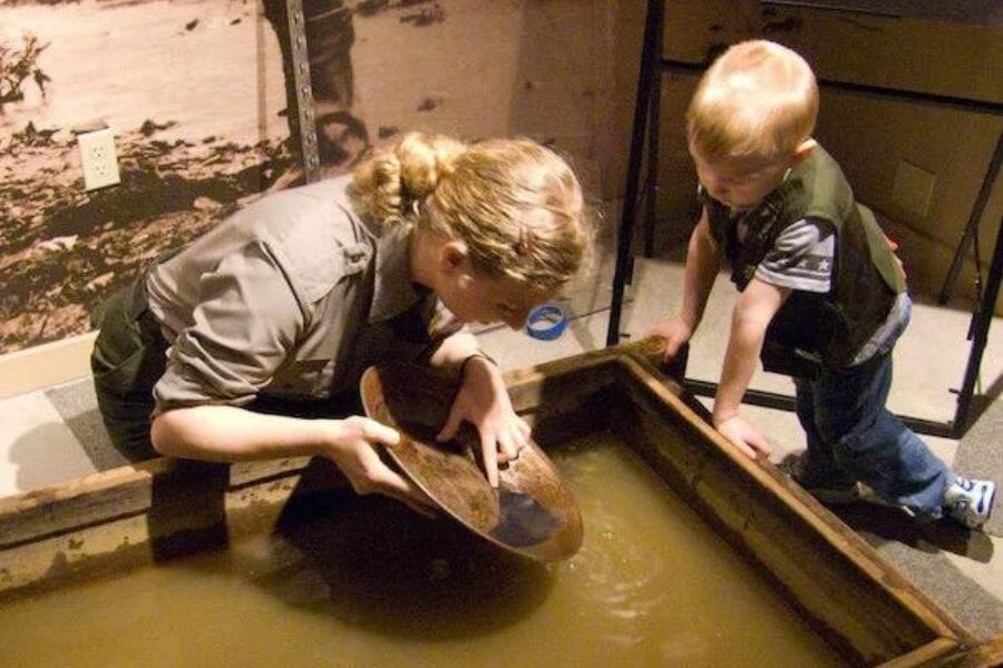 A staff of Klondike Gold Rush National Historic Park showing a kid how to pan for gold