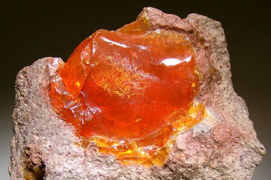A bright, translucent sample of an orange Fire Opal atop a rock