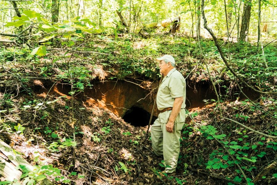 A prospector standing near an excavation dug in Hog Mountain