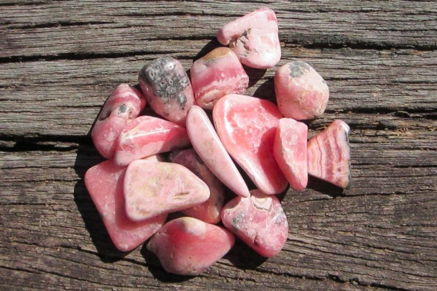 A bunch of irregularly shaped pink Rhodochrosite crystals on wooden surface