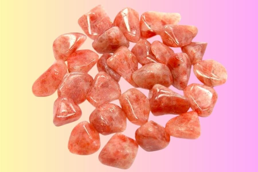 A bunch of shiny, polished candy orange Sunstone crystals on pink and yellow background