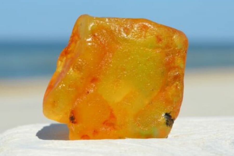 A vibrant amber crystal sitting on a white smooth surface