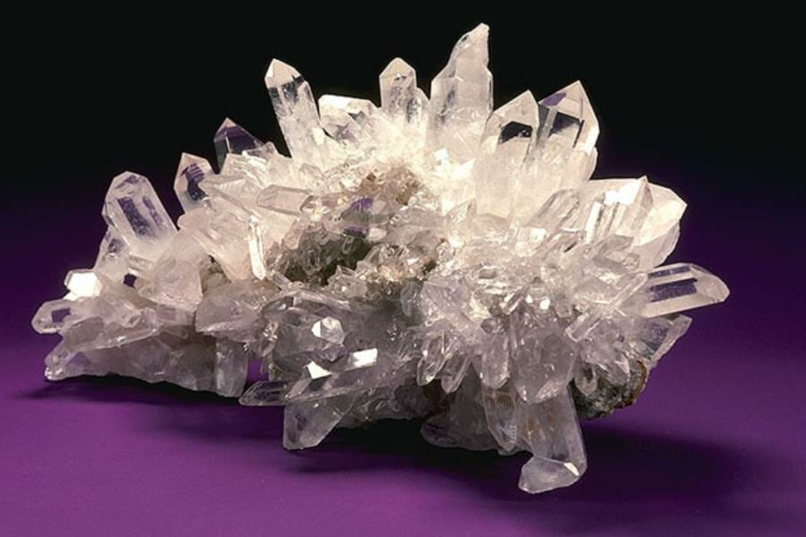 A dramatic cluster of white and clear crystals on a purple background