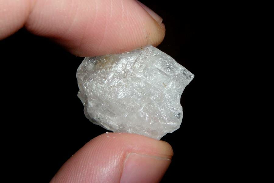 A small white crystal held between a thumb and forefinger