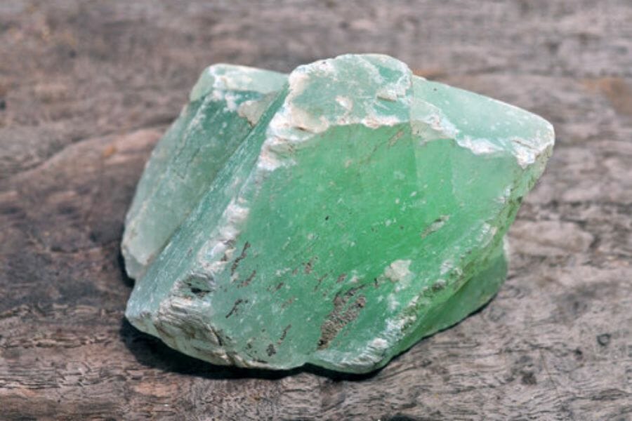 A dazzling jade crystal with an uneven smooth surface sitting on a rock