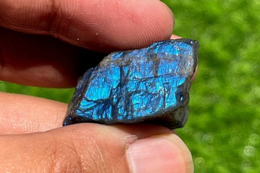 A tiny shiny labradorite with a metallic sheen held between two fingers