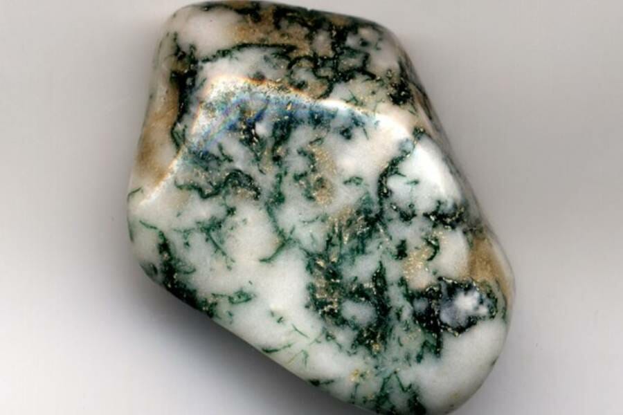 A palm-sized chunk of moss agate that is white with green and gold flecks and patterns