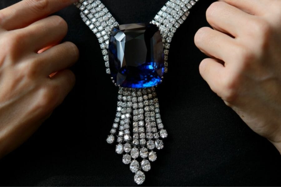 Two hands handling the Blue Belle of Asia, a necklace encrusted with small white diamonds and a huge cushion-cut Sapphire