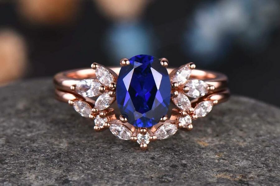 A breathtaking photo of a golden ring studded with small white diamonds and a jaw-dropping piece of oval Blue Sapphire