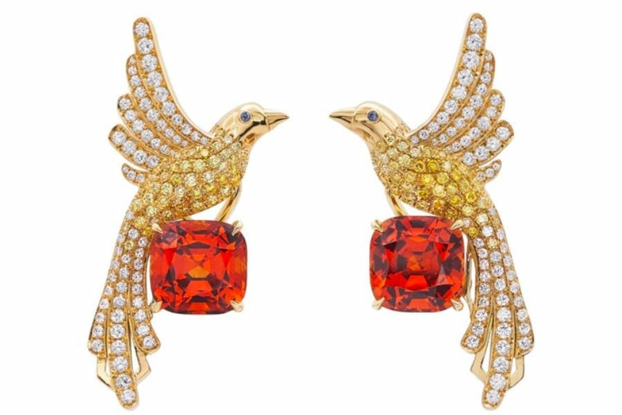 A pair of earrings shaped like two birds each carrying a faceted orange Garnet