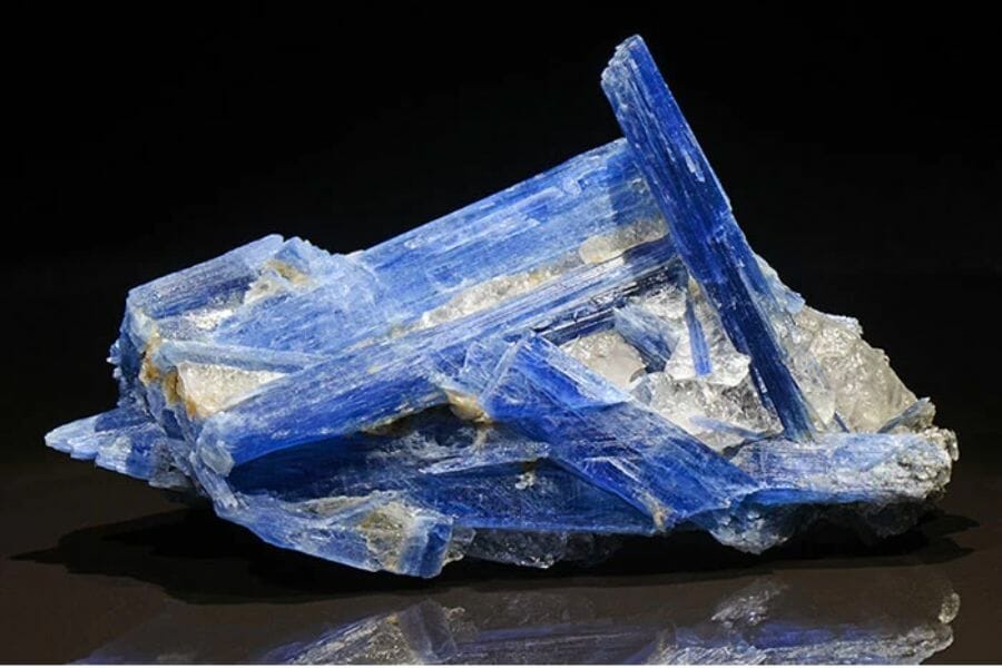 A sample of blue Kyanite and clear white Quartz crystals on a black surface