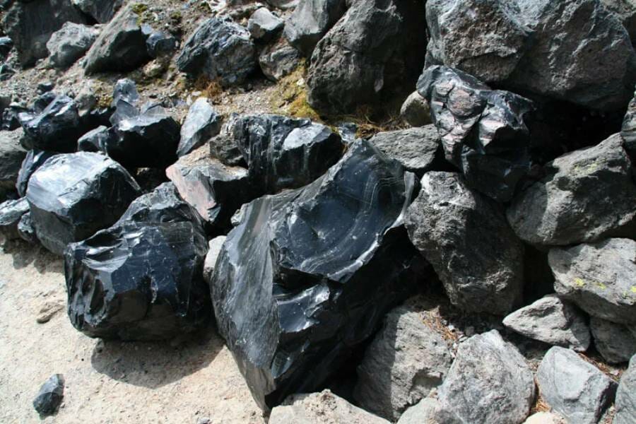 Dozens of small black chunks of obsidian lying on the sand.