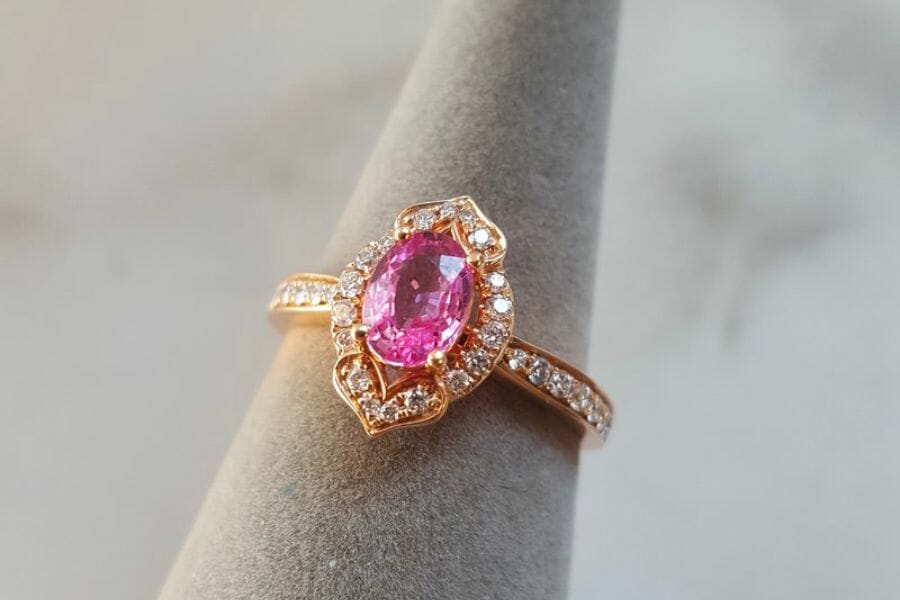 A close up look at a sparkling Pink Sapphire surrounded by white diamonds in a golden ring
