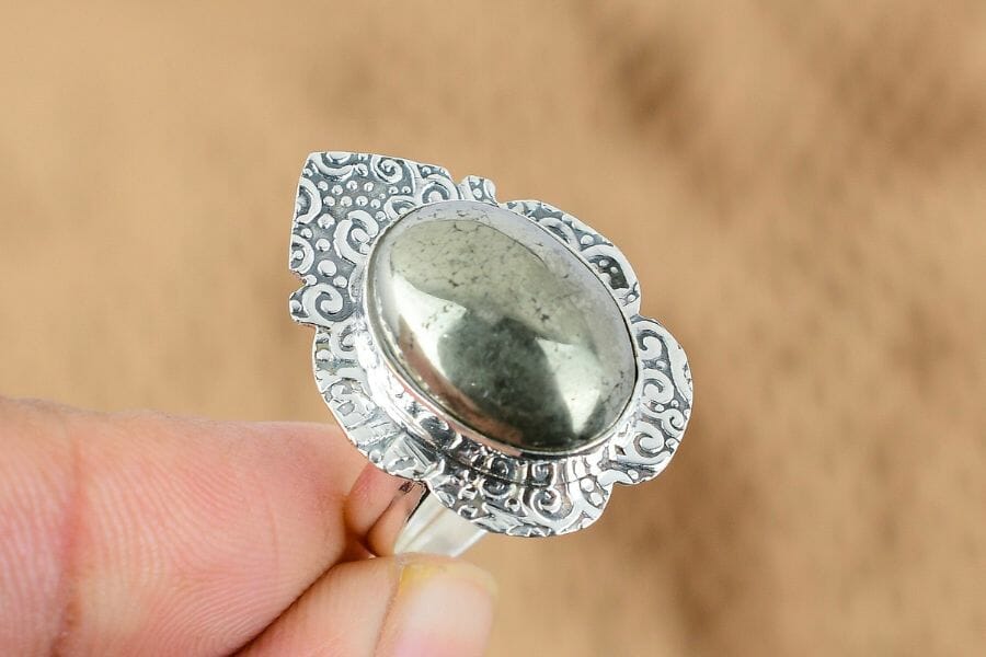 A beautiful piece of Pyrite Cabochon set on an intricate silver ring held by two fingers