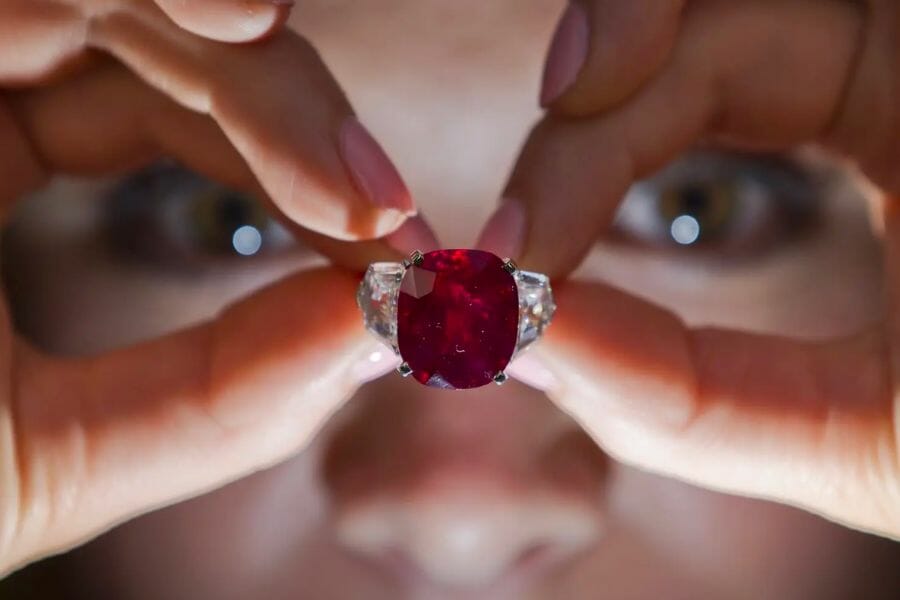 The stunning Sunrise Ruby set on a ring with diamonds on the side held by a person on eye level