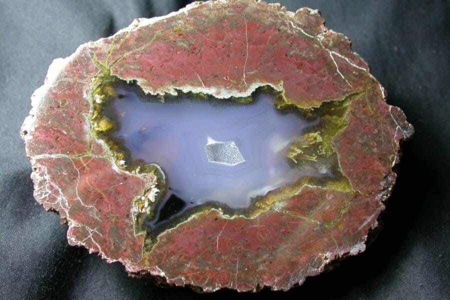 A stunning red rock thunder egg filled with a milky blue crystal that looks like a lake