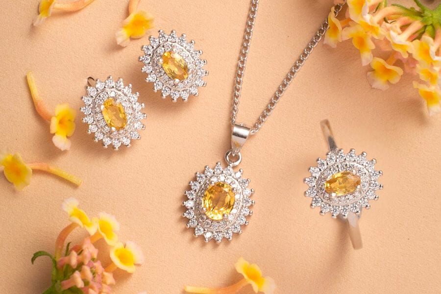 A silver jewelry set of necklace, earrings, and rings adorned with oval Yellow Sapphires