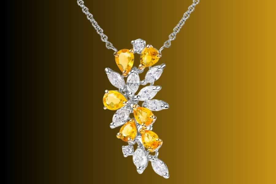 A close up look at a silver pendant encrusted with white diamonds and yellow sapphires