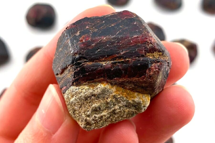 A raw, red Garnet (Almandine) attached to a rock held by hand