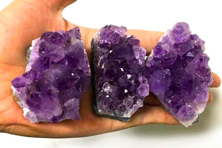 Three clusters of deep purple Amethyst held by a hand