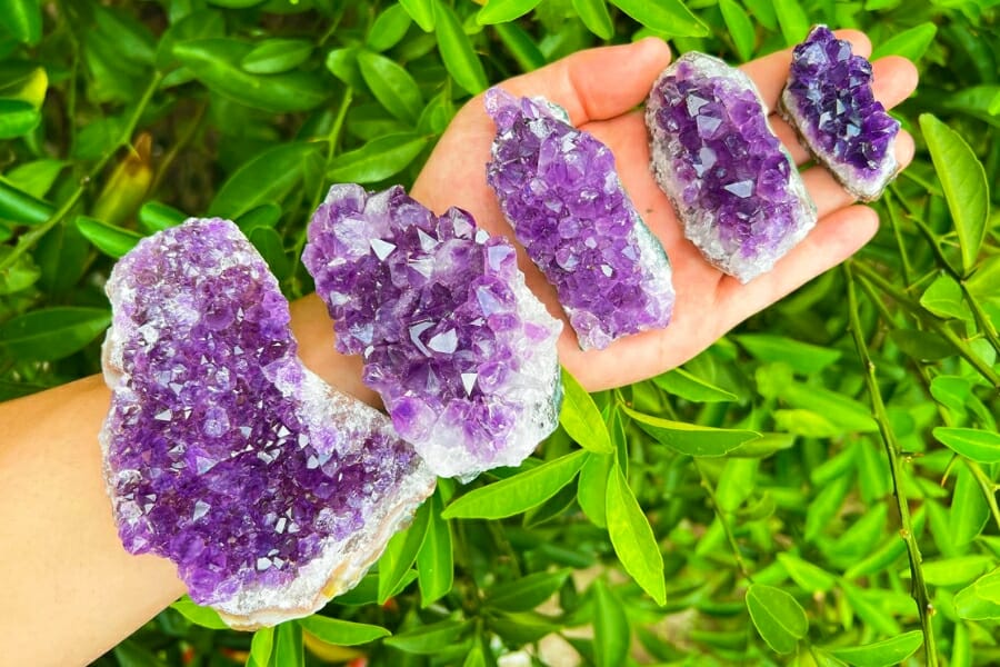 A single hand stretch out while holding 5 clusters of Amethyst crystals in varying sizes