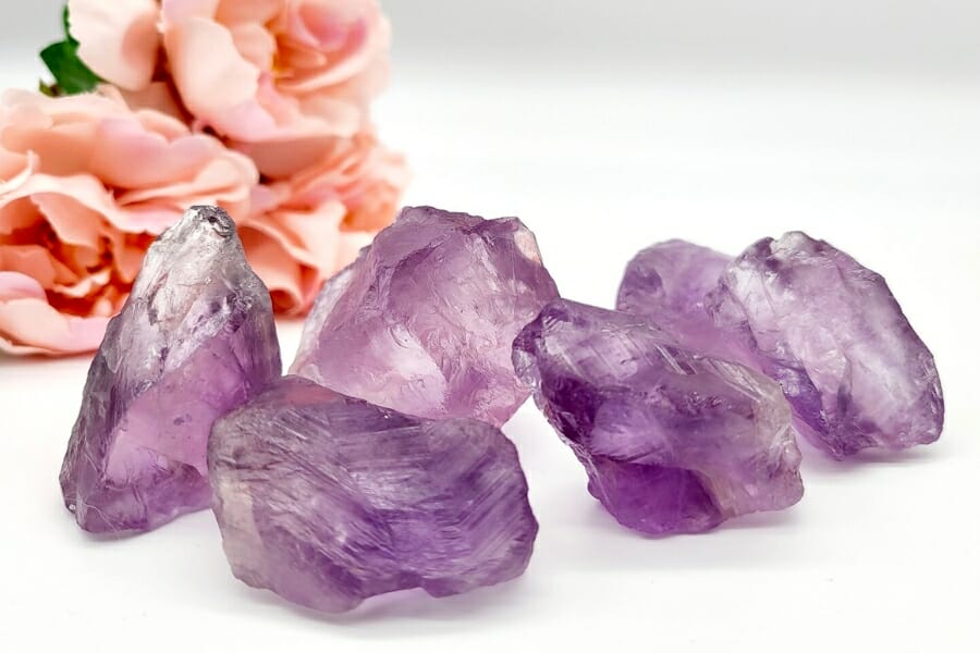Four raw purple Amethys crystals with a peach rose on the background