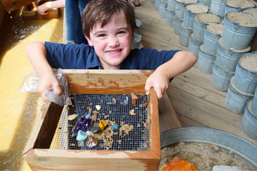 A young boy smiling from ear-to-ear showing the gems he found in the sluice of Greenville Gemstone Mine