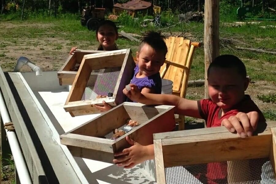 Three kids proudly smiling and showing their finds at the sluice of Cedar Panning