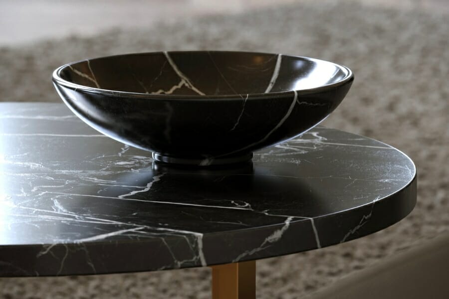 A fruit bowl on top of a table both made out of black Nero Marquina marble with white veins