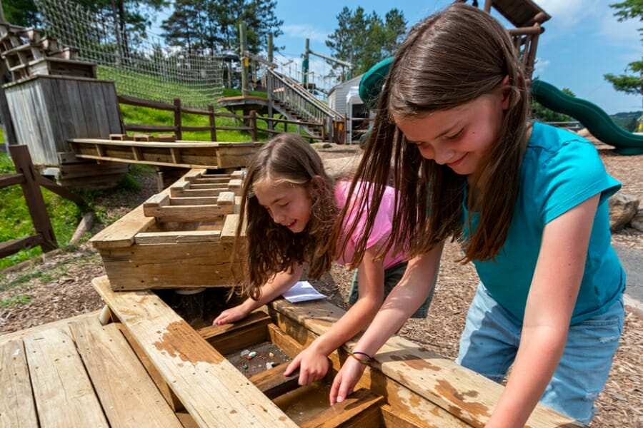 Two girls smiling as they sift through dirt for gems at the sluice of Marsh Mountain Mining Company