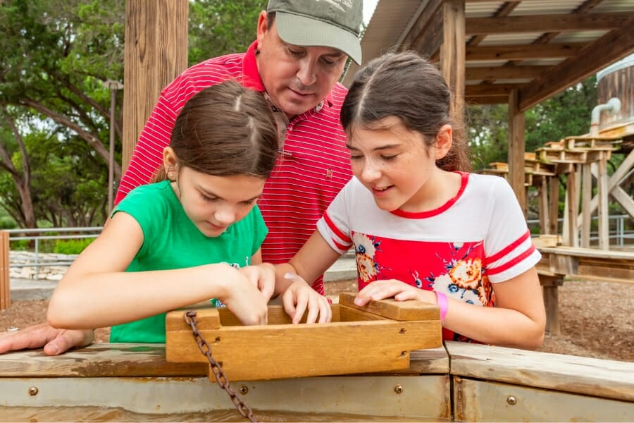 Two young girls with their dad happily sorting through their finds at the sluice of Natural Bridge Caverns
