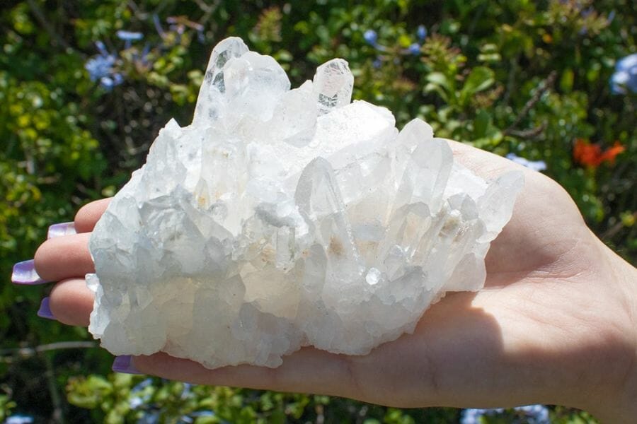 Gorgeous white quartz crystal held on a hand with leaves in the background