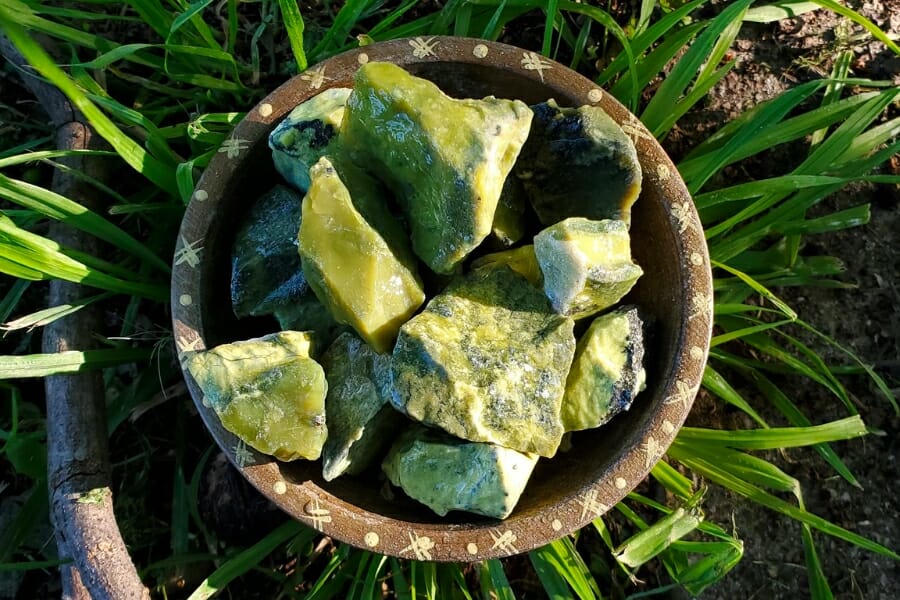 A bunch of raw, yellow green Serpentine in a wooden bowl on a grassy ground