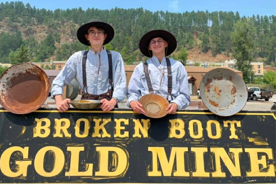 Two teenage boys posing with their gold pans at the Broken Boot Gold Mine signage