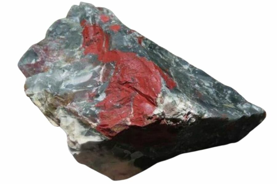An enormous bloodstone with red hues and gray minerals sitting on a wooden surface