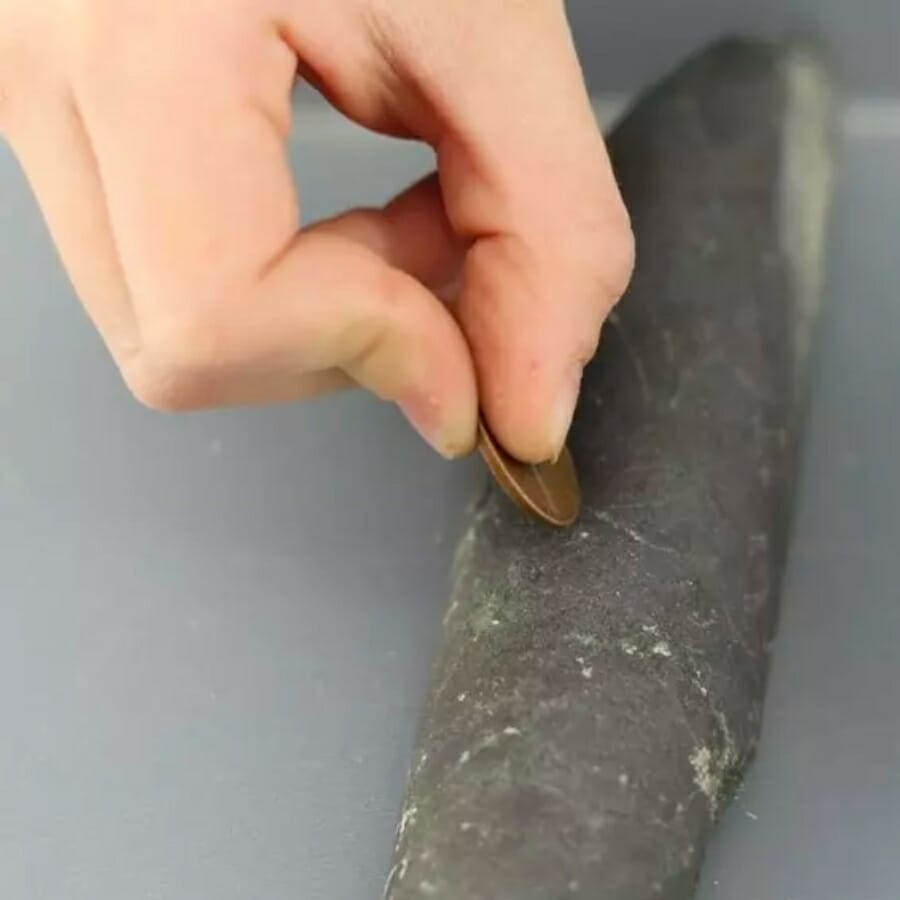 A hand scratches coin agains a specimen laid on a gray background