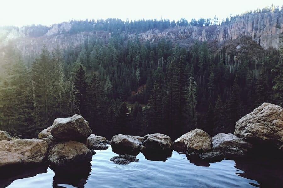 Rocky hot springs at the mountain with a view of tall green trees and cliffs 