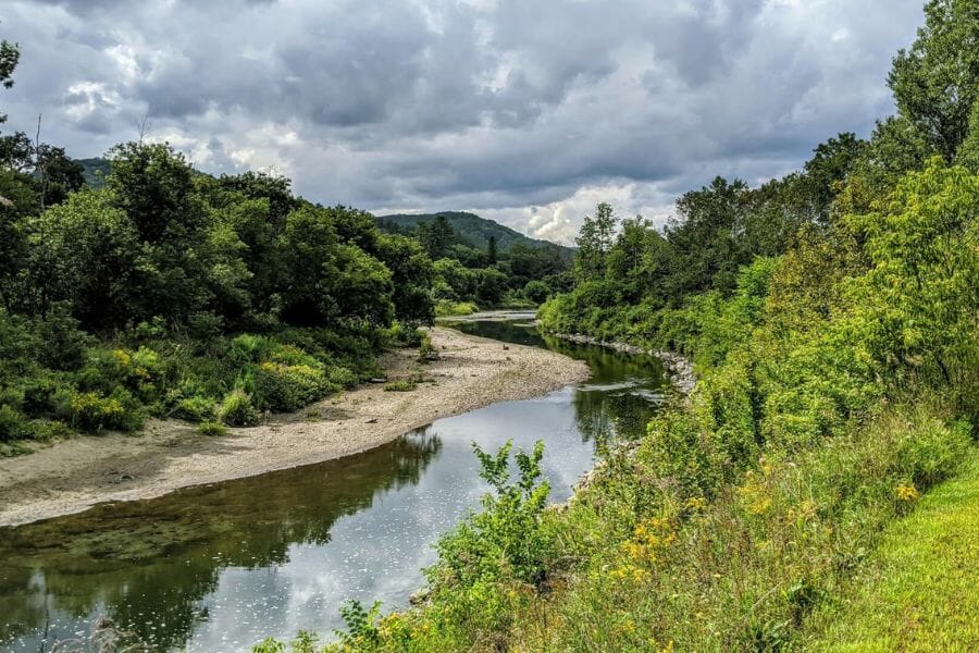 A nice and tranquil Ottaquechee River with nice lush trees on both sides and looming dark clouds above