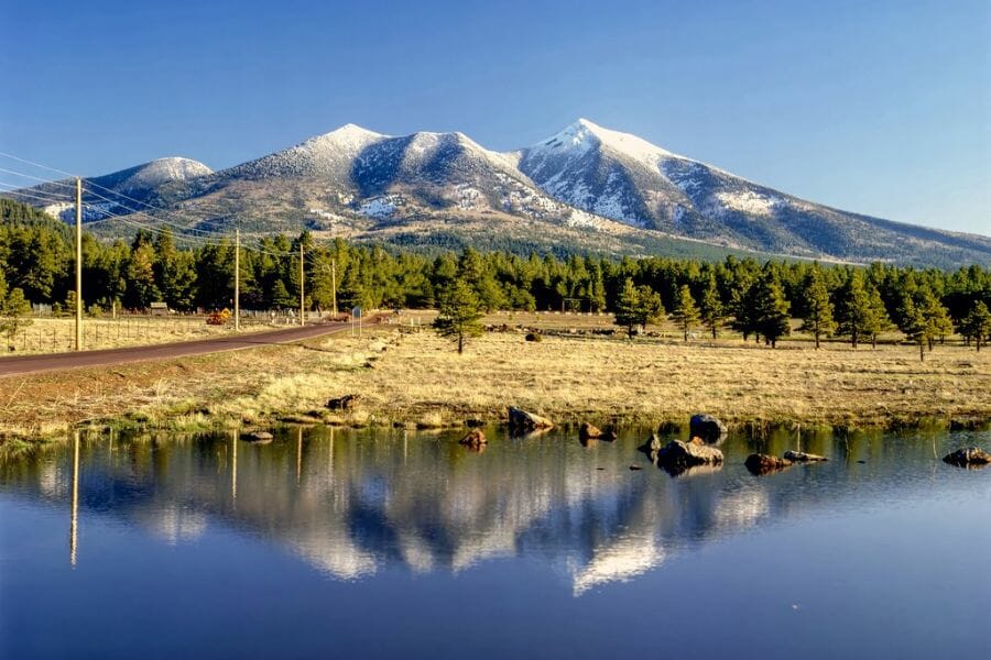 A picturesque view of the San Francisco Peaks with snowy tops and a lake at the bottom