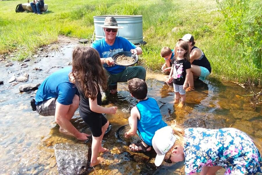 A man proudly smiles around kids who are also gold panning at South Pass City