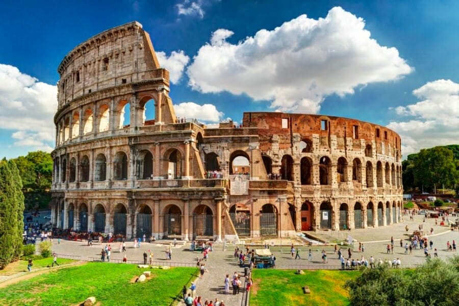 A picture of The Colosseum, made of Travertine, with visitors roaming outside