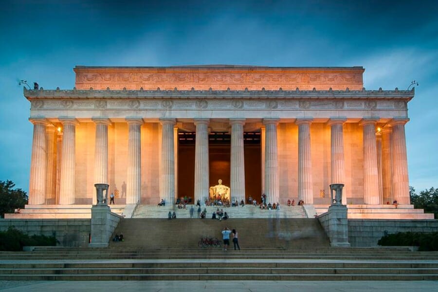 The Lincoln Memorial, made of Limestone, during night time with visitors on its entrance steps