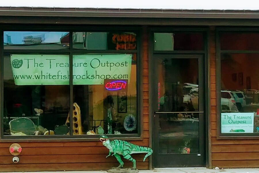 Front store window of Treasure Outpost Rock Shop with a small dinosaur figurine beside the door