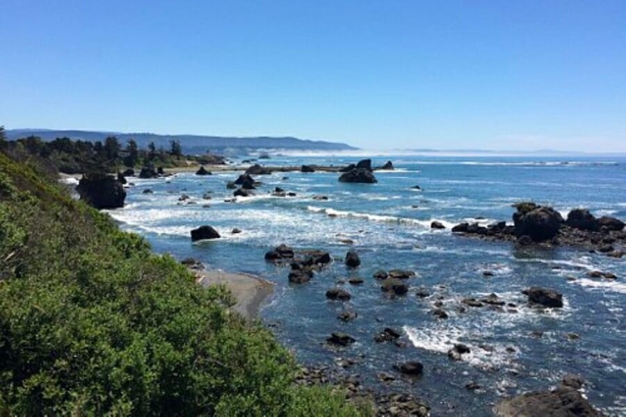 Aerial view of a beach in Crescent City with strong waves and rock formations