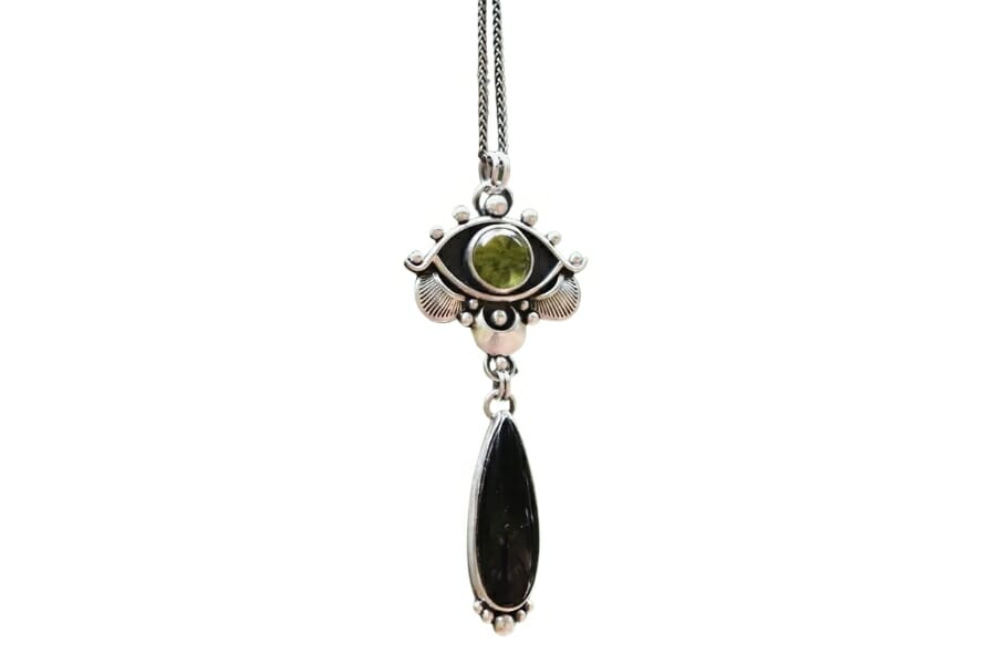 A green evil eye pendant with an onxy teardrop hanging below it